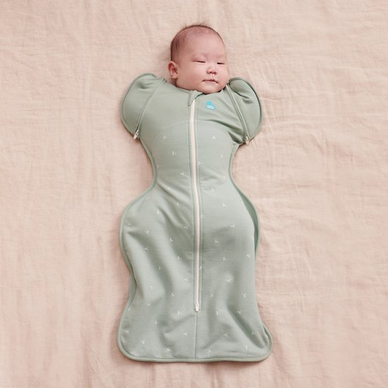 Baby in lichtgroene omslagdoek met twijgjespatroon en ritssluiting, met armen naar beneden.