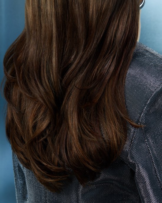 Close-up van golvend bruin haar met highlights, gedragen over een glinsterende zilveren jas.