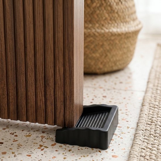 Een zwarte deurstop met ribbels onder een houten meubel.