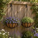 Twee hangende bloempotten met kettingen aan een houten schutting. De linkerpot is gevuld met paarse bloemen, de rechterpot met groene planten.