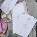 Kind met roze geruite jurk tekent poppetjes met Kidywolf stiften op tafelkleed.