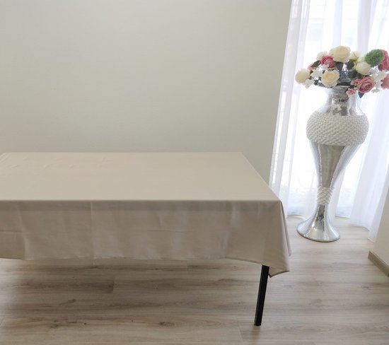Een lichtbeige tafelkleed van 140x240 cm op een tafel naast een vaas met bloemen.