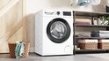 Witte Bosch Serie 6 wasmachine met zwarte deurrand, naast een kledingkast met wasgoed.