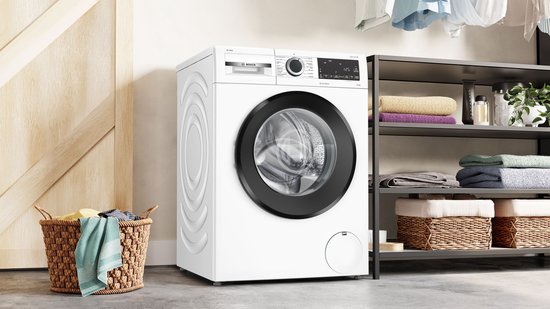 Witte Bosch Serie 6 wasmachine met zwarte deurrand, naast een kledingkast met wasgoed.