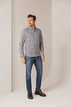 Man draagt een blauw overhemd met een fijne print van witte, bruine en donkerblauwe lijntjes. Hij draagt er een jeans bij.