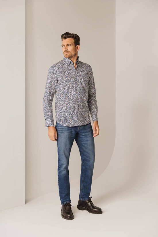 Man draagt een blauw overhemd met een fijne print van witte, bruine en donkerblauwe lijntjes. Hij draagt er een jeans bij.