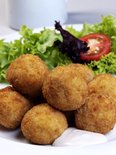 Goudbruine kroketten met een salade en tomatenschijf op een wit bord.