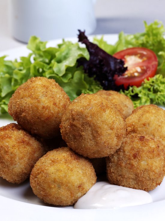Goudbruine kroketten met een salade en tomatenschijf op een wit bord.