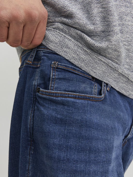 Detail van de voorzakken van een spijkerbroek van blauw denim met oranje stiksels.