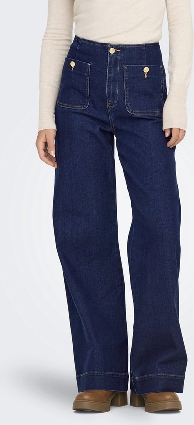 Onderlichaam van een vrouw in donkerblauwe spijkerbroek met wijde pijpen en beige coltrui.