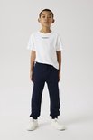 Jongen in een witte T-shirt met tekst 'Studio Edition' en een donkerblauwe joggingbroek, met witte sneakers.