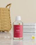 Fles SteamStory "Ruby" wasparfum op een marmeren tafel met een mand en stapel handdoeken op de achtergrond.