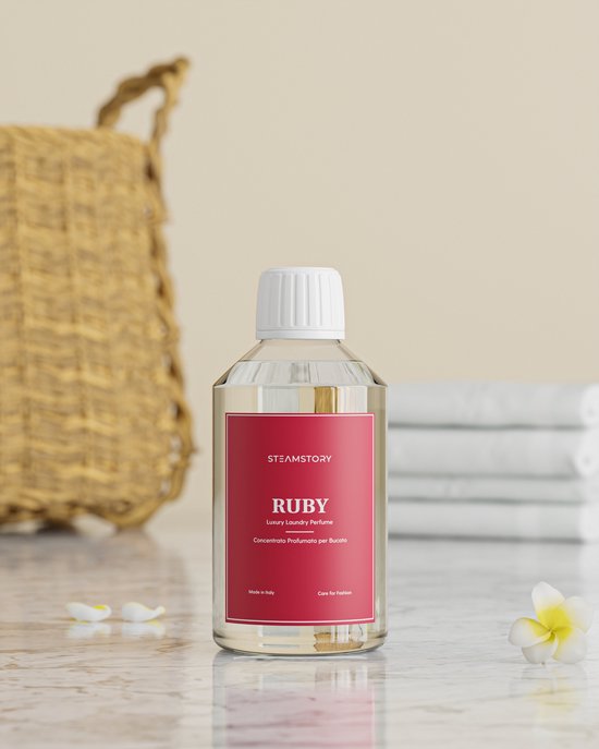 Fles SteamStory "Ruby" wasparfum op een marmeren tafel met een mand en stapel handdoeken op de achtergrond.