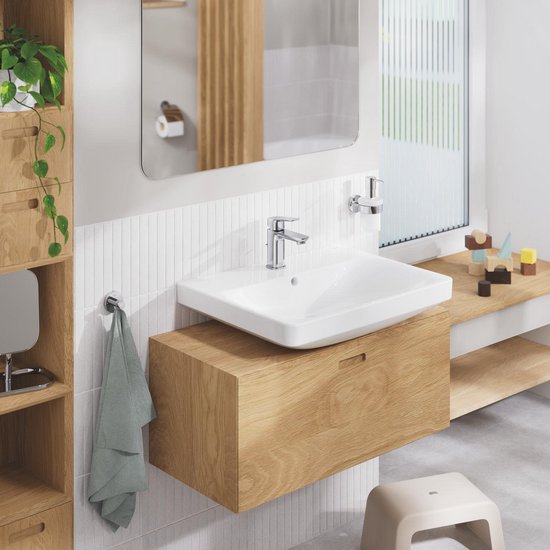 Chroomkleurige zeepdispenser aan de muur naast een wastafelmeubel van hout.