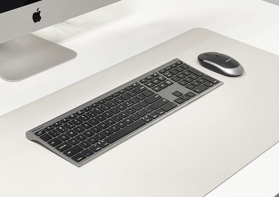 Een zilverkleurig draadloos toetsenbord en muis op een lichte mat naast een Apple iMac.