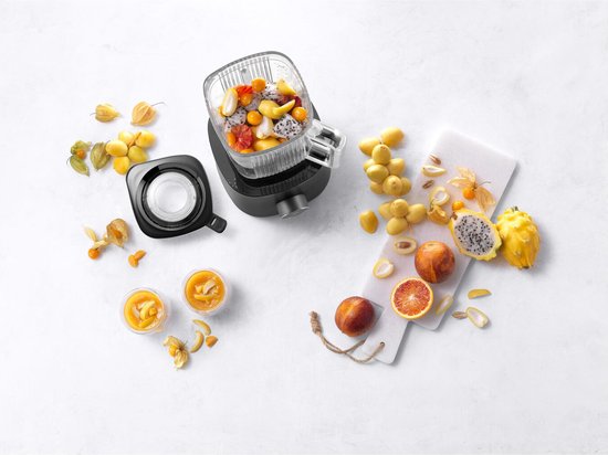 Pichet de blender rempli de fruits, deux verres de smoothie et des fruits à côté.