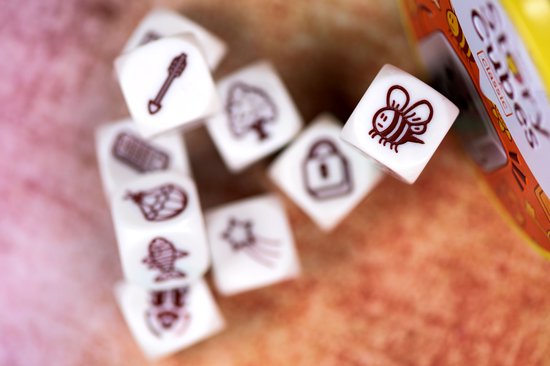 Witte dobbelstenen met bruine afbeeldingen van een bij, ster, slot, boom, vogel, en een speer, op een oranje ondergrond.