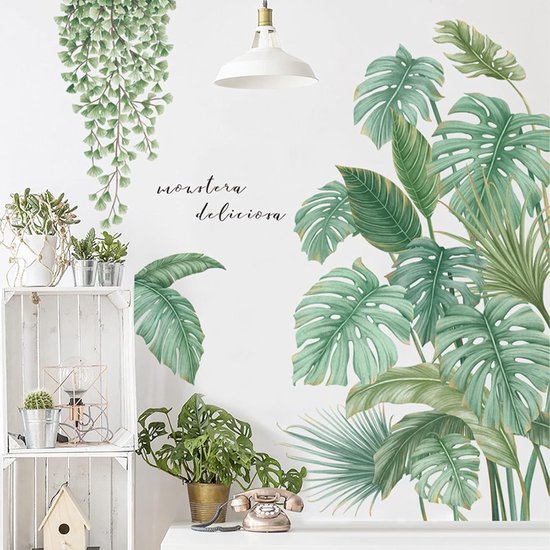 Een muursticker met groene Monstera deliciosa bladeren en hangende varens boven een witte kast met planten en decoratie.