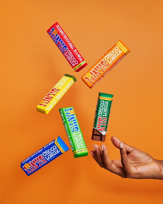 Hand reikt naar vijf Tony's Chocolonely repen die in de lucht zweven: rood, oranje, geel, groen en een half opgegeten reep.