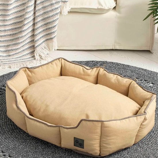 Panier rectangulaire beige pour animaux de compagnie avec bords surélevés et souples, sur un tapis gris à côté d'un canapé.