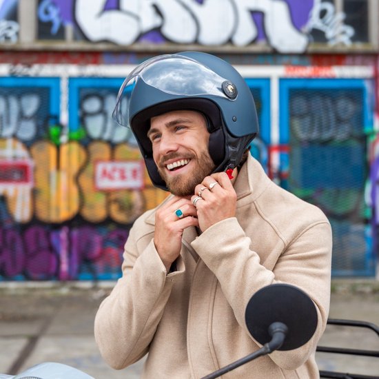 Man met donkerblauwe helm met vizier en beige jas, die de kinband vastklikt.