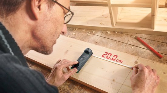 Man meet een stuk hout met de Bosch Zamo afstandsmeter en lintadapter, 20.0 cm wordt weergegeven.