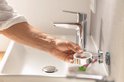 Une main saisit un support blanc avec des pilules, à côté d'un lavabo blanc et d'un robinet.