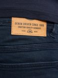Detail van een leren label op een donkerblauwe jeans met tekst: 'DENIM DRIVEN SINCE 1989 CRAFTING QUALITY GARMENTS'.