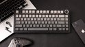 Zwart toetsenbord met grijze toetsen, naast een laptop, smartphone en controller.