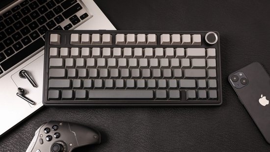 Zwart toetsenbord met grijze toetsen, naast een laptop, smartphone en controller.