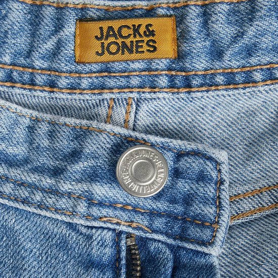 Detail van de tailleband van een spijkerbroek met een oranje Jack & Jones label en een zilveren knoop.