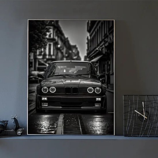 Zwart-wit canvasposter van een klassieke BMW E30 M3 sportwagen, laag bij de grond, op een natte straat in een stedelijke omgeving. Ronde koplampen.