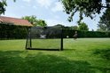 Jongen schiet voetbal op een zwart EXIT doel in een groene tuin.