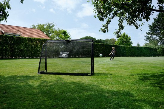 Jongen schiet voetbal op een zwart EXIT doel in een groene tuin.