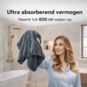 Femme en chemisier bleu clair nettoyant une paroi de douche vitrée avec une lingette microfibre gris foncé.