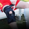 Man op gras die een zwarte Zamst ZK-X kniebrace met scharnieren past.