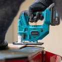 Hand met grijze werkhandschoen houdt turquoise ProXtar decoupeerzaag met accu tijdens het zagen van een dun stuk materiaal.