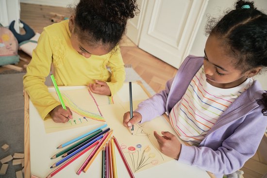 Twee meisjes tekenen met kleurpotloden op papier, een van hen draagt een paarse hoodie.