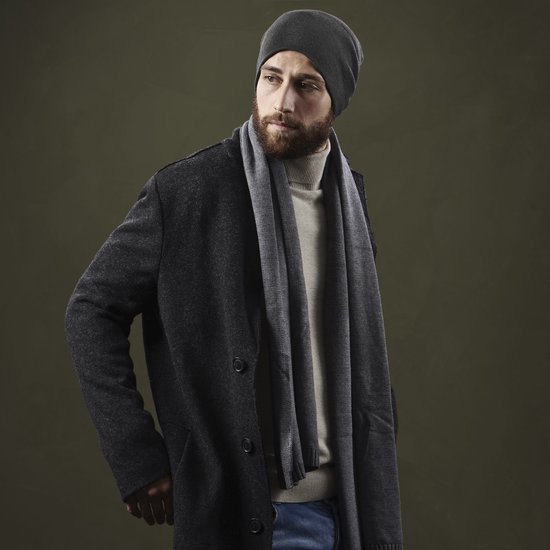 Man met baard draagt een grijze beanie muts, sjaal, coltrui en jas.
