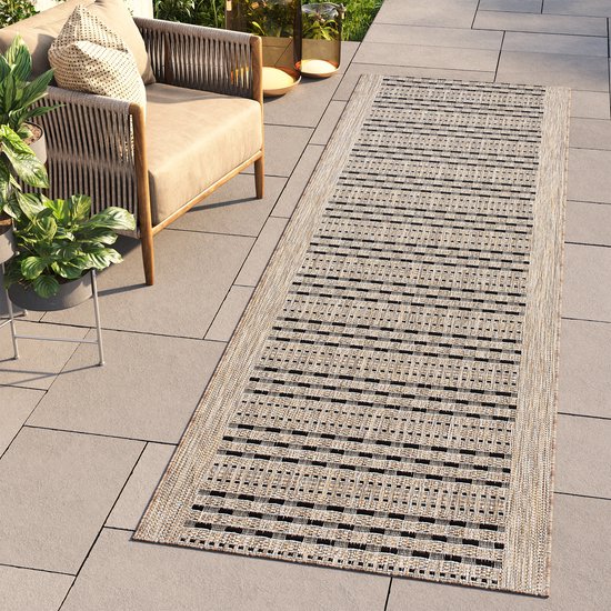 Tapis de passage beige à rayures noires, posé sur une terrasse près d'un fauteuil.