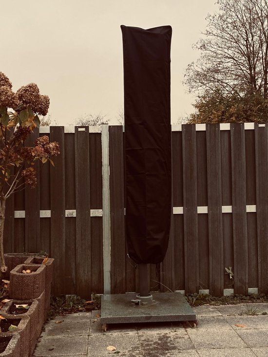 Zwarte parasolhoes, volledig gesloten, staand op een voet, tegen een houten schutting.