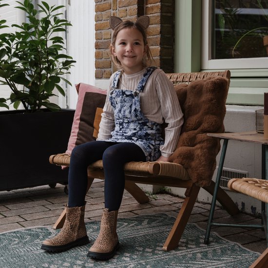 Meisje met kattenoren, zittend op een stoel, met panterprint chelseabootjes aan.