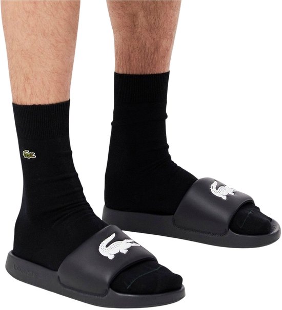 Man met zwarte sokken en zwarte Lacoste slippers met witte krokodil.