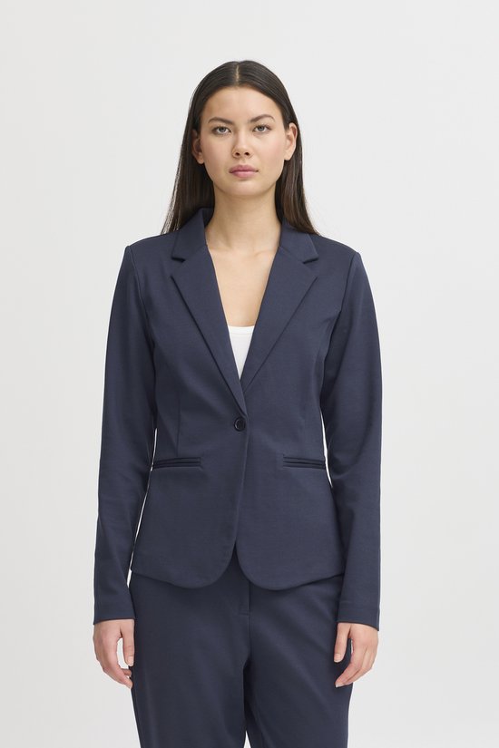 Model in een getailleerde donkerblauwe blazer met een enkele knoop en een witte top.