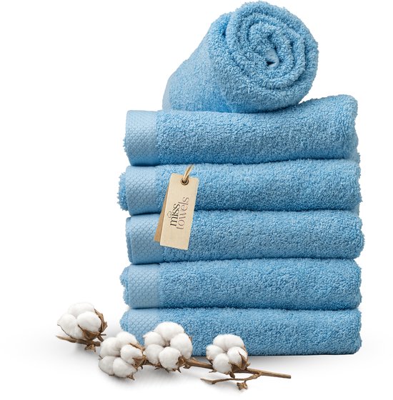 Pile de serviettes bleu clair avec un rouleau et une étiquette, avec une branche de coton sur fond noir.