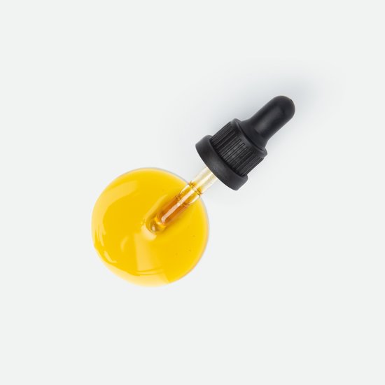 Een druppel glanzende gele CBD-olie met een glazen pipet op een witte achtergrond.