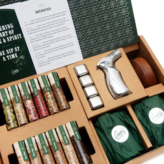 Boîte ouverte avec 12 tubes en verre de produits botaniques, un verre à whisky et des pierres à whisky argentées.