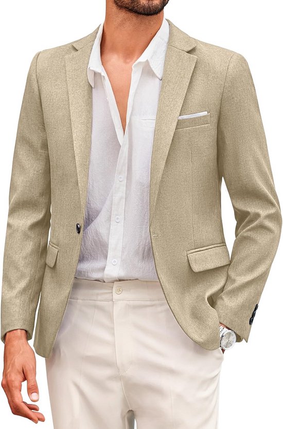 Man met beige blazer, witte blouse en crème broek, hand in zak, horloge zichtbaar.