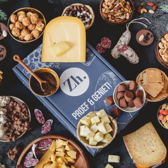 Een kaasplank met kaas, worstjes, noten, koekjes, chocolade en een blauwe 'Proef & Geniet!' doos.