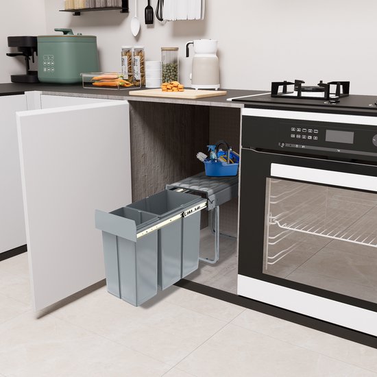 Grijze uittrekbare dubbele afvalbak, geïnstalleerd in een keukenkast naast een oven, met een schoonmaakset bovenop.
